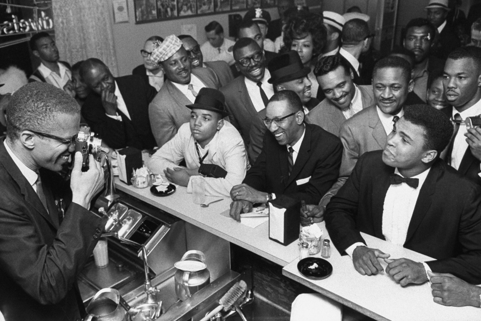 MARCH 1964 - MIAMI: Black Muslim leader Malcolm X (L) behind soda fountain training his camera on tux-clad Cassius Clay (now Muhammad Ali) (R) sitting at counter surrounded by jubilant fans after he beat Sonny Liston for the heavyweight championship of the world.  (Photo by Bob Gomel/The LIFE Images Collection via Getty Images/Getty Images)